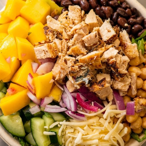 Close-up of a colorful salad bowl with chicken, mango, black beans, chickpeas, and vegetables.