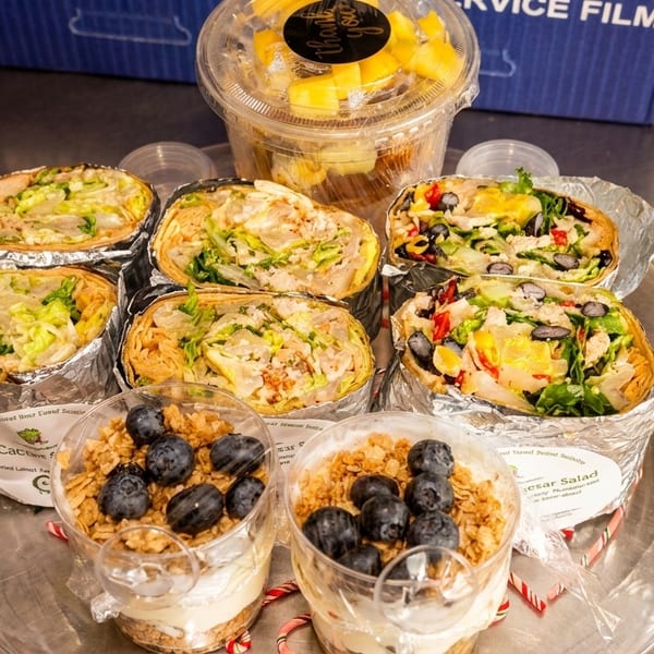 A catering tray with various wraps, fruit cups, and parfaits with blueberries and granola.